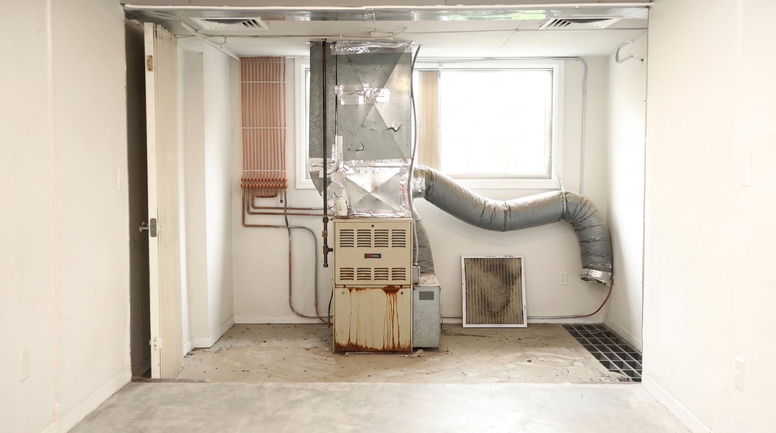 A basement closet with a rusted 1990s gas furnace and sagging flex duct